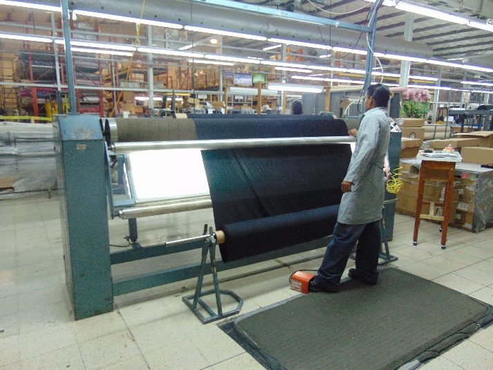 A technician running a roll of dark fabric through an inspection machine.
